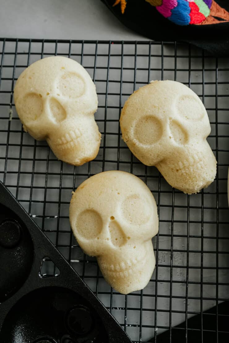 Three mini lemon sugar skull cakes cooling on a wire rack after baking.
