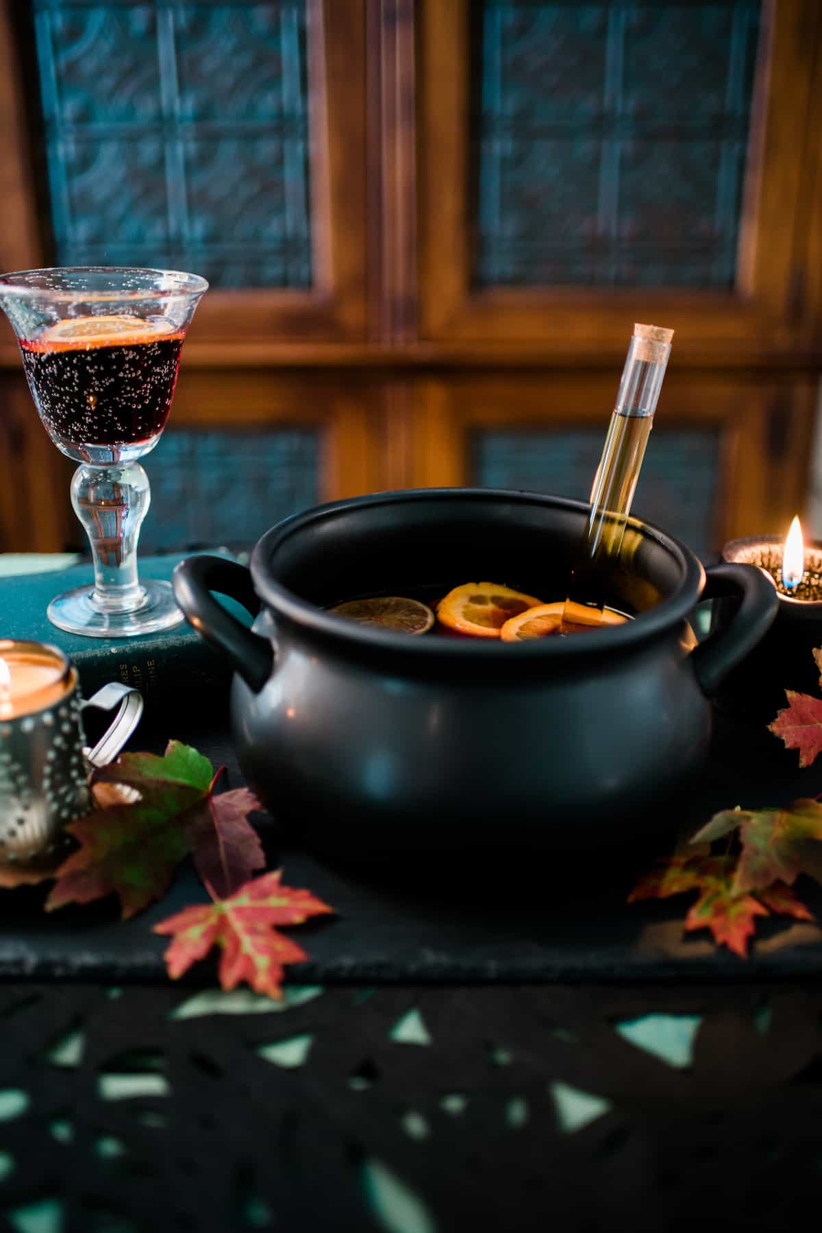 halloween tablescape with a black witches cauldron filled with halloween sangria and a test tube of liquor plus fall leaves and lit candles.