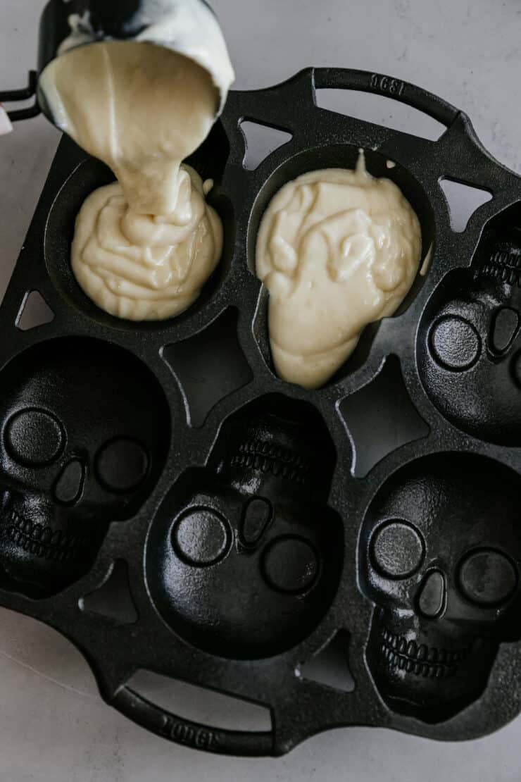 Scooping lemon cake batter with a disher into a skull cake pan mold.