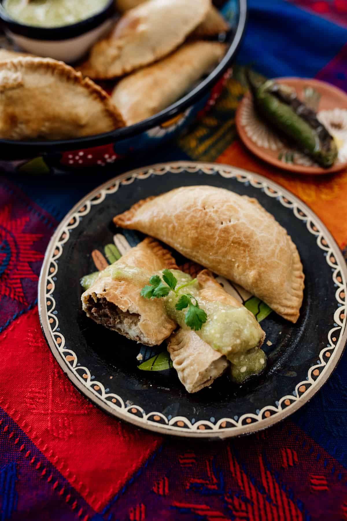 open empanada on a Mexican black plate filled with Mexican picadillo drizzled with salsa verde. 