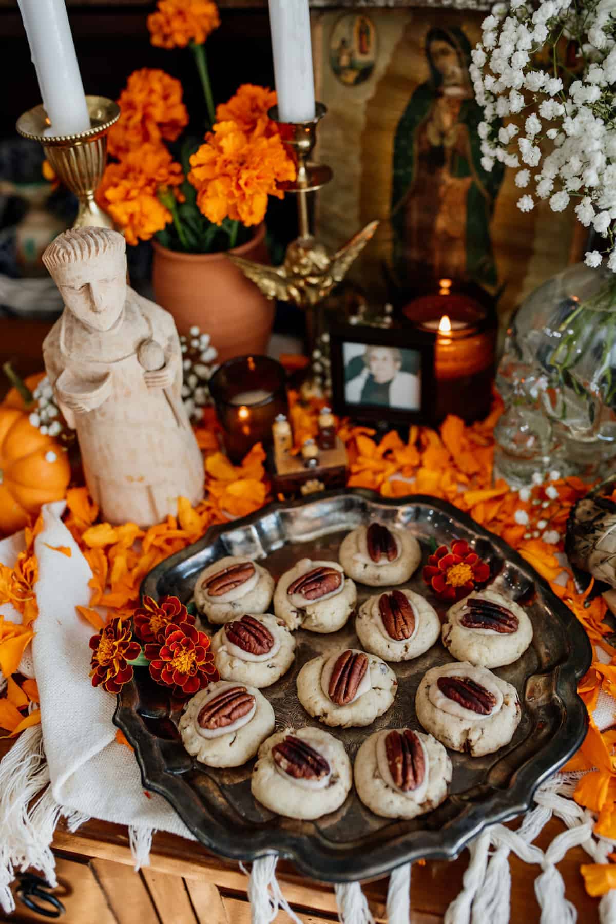 Double Pecan Thumbprint cookies on an altar for day of the dead with a patron saint Pasquale and marigolds .
