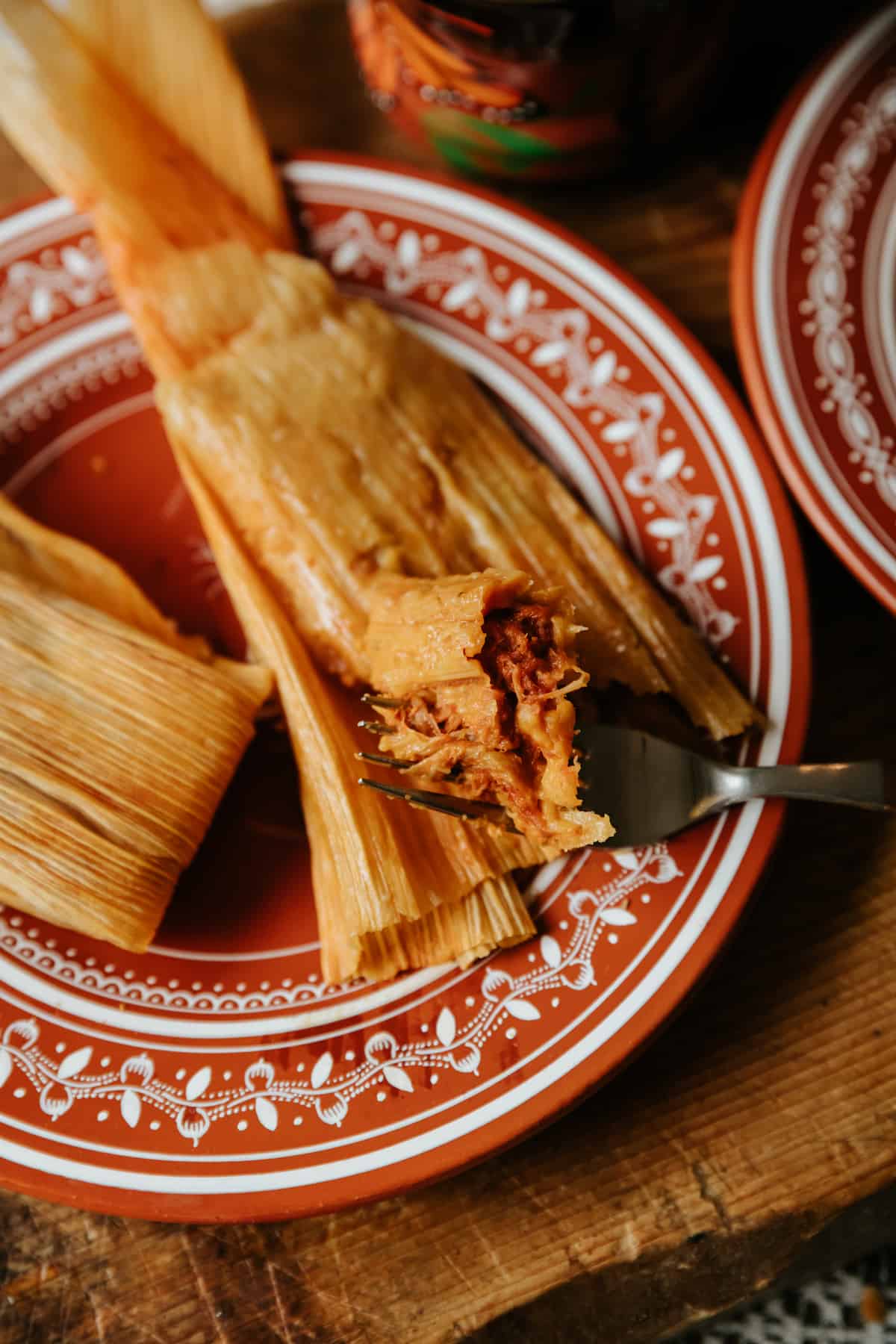 plate with two pork tamales rojos with a fork taking a bite. 