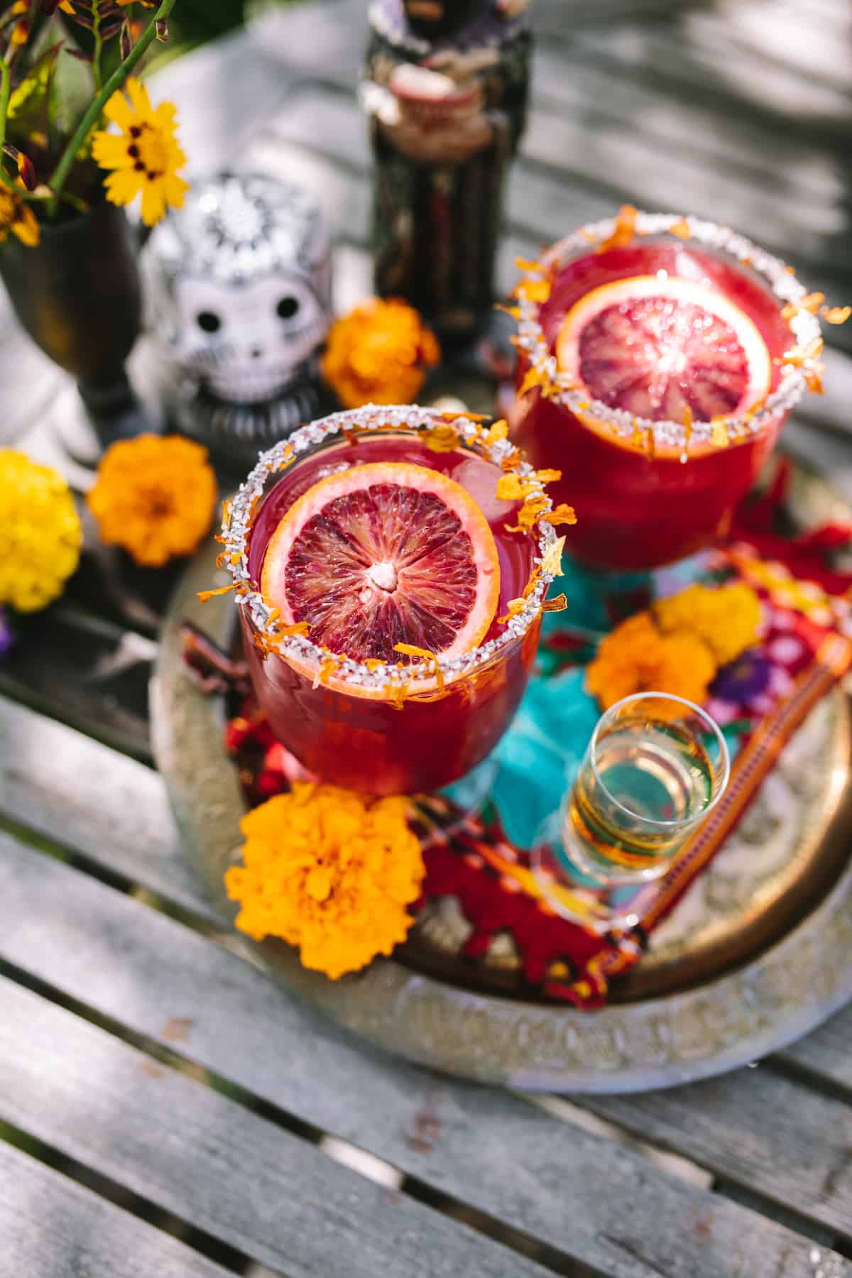 45 degree angle shot of two marigold blood orange margaritas with a salt and marigold petal rim.