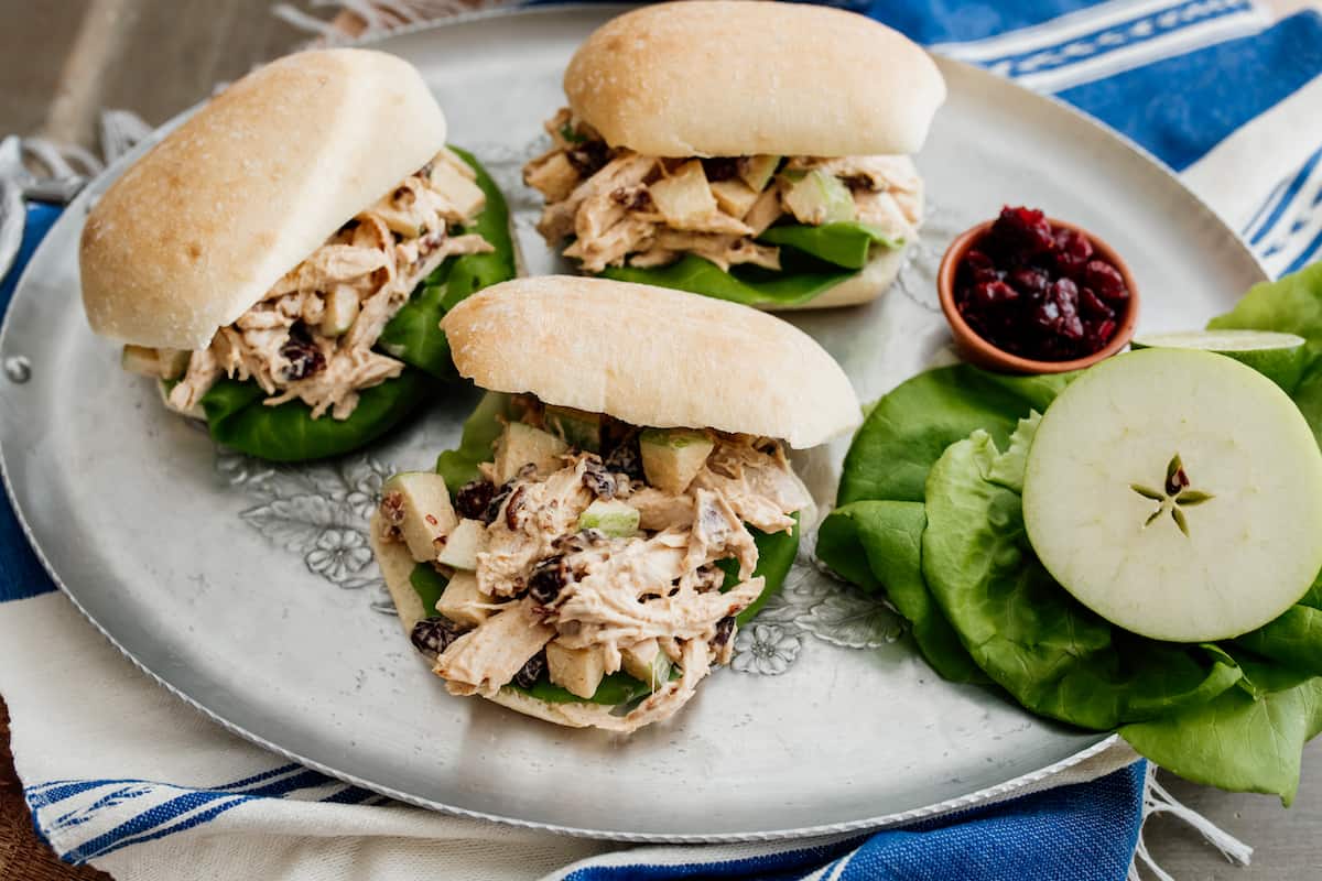 chicken salad with apples, pecans, and cranberries on ciabatta rolls on a silver platter.