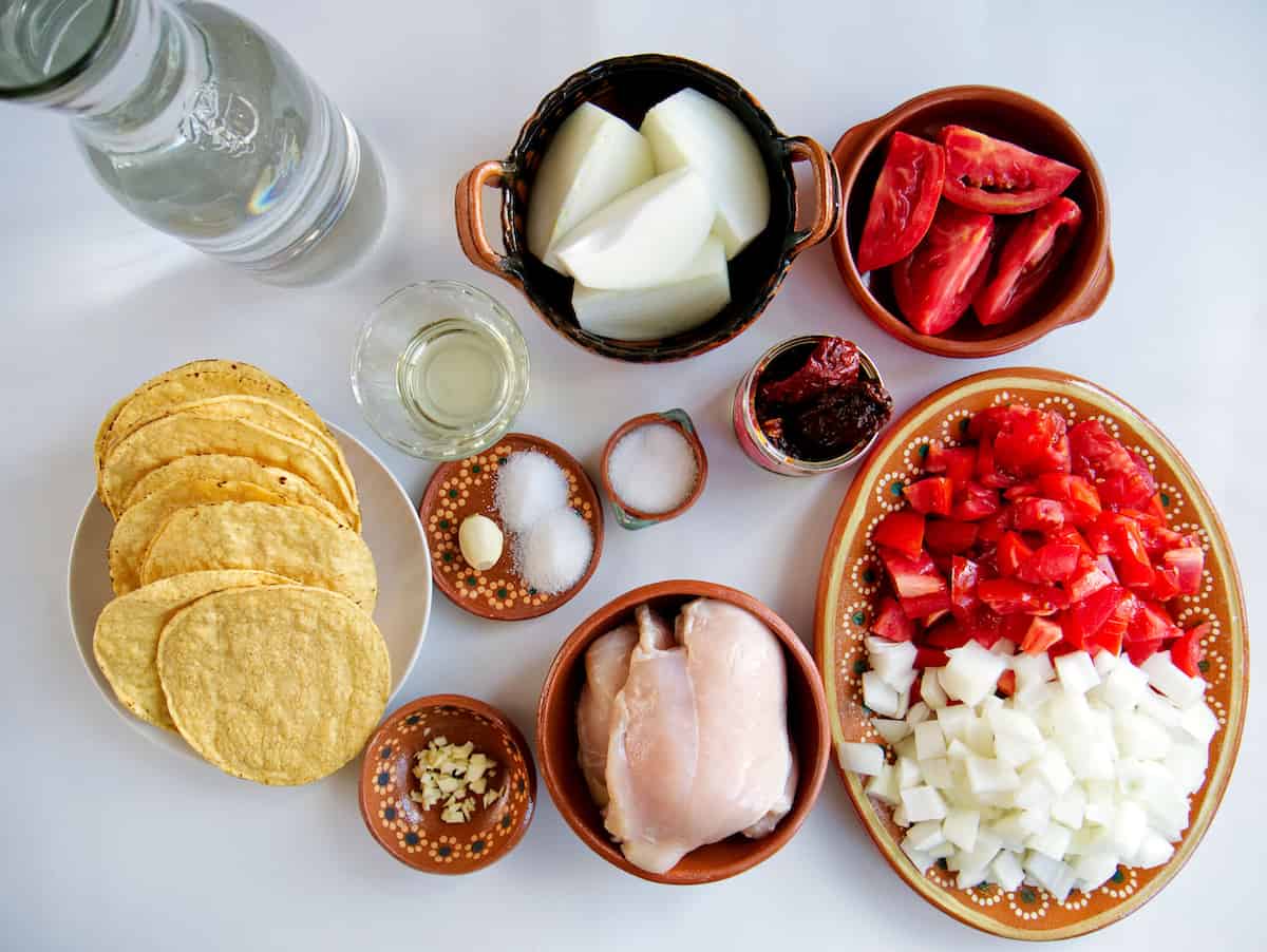 overhead shot of ingredients for making instant pot chicken tinga tostadas measured out in bowls on a white table. 
