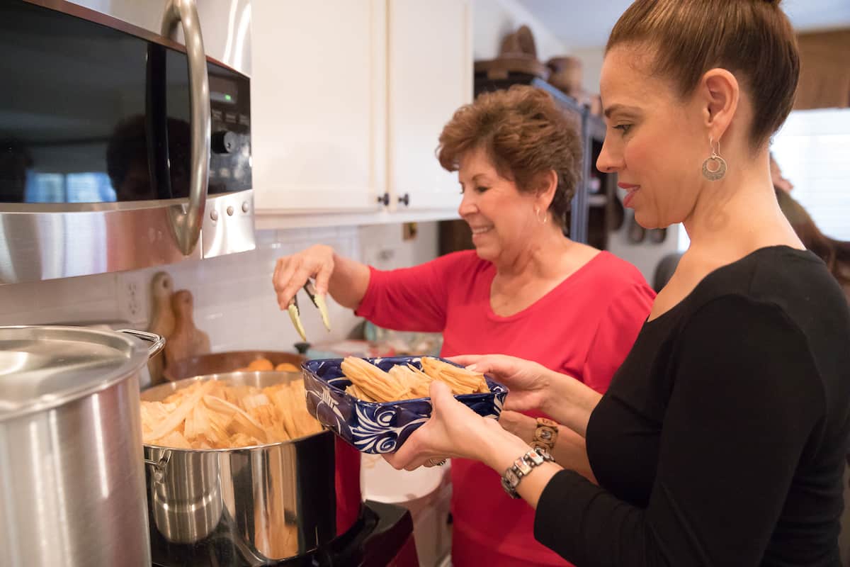 Latina women mother and daughter in the kitchen making tamales at a tamalada.