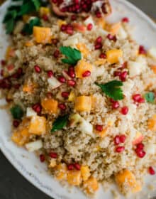 closeup hero shot of roasted butternut squash quinoa salad flecked with pomegranate arils and garnished with fresh parsley.