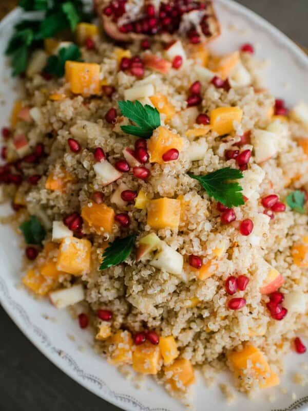 closeup hero shot of roasted butternut squash quinoa salad flecked with pomegranate arils and garnished with fresh parsley.