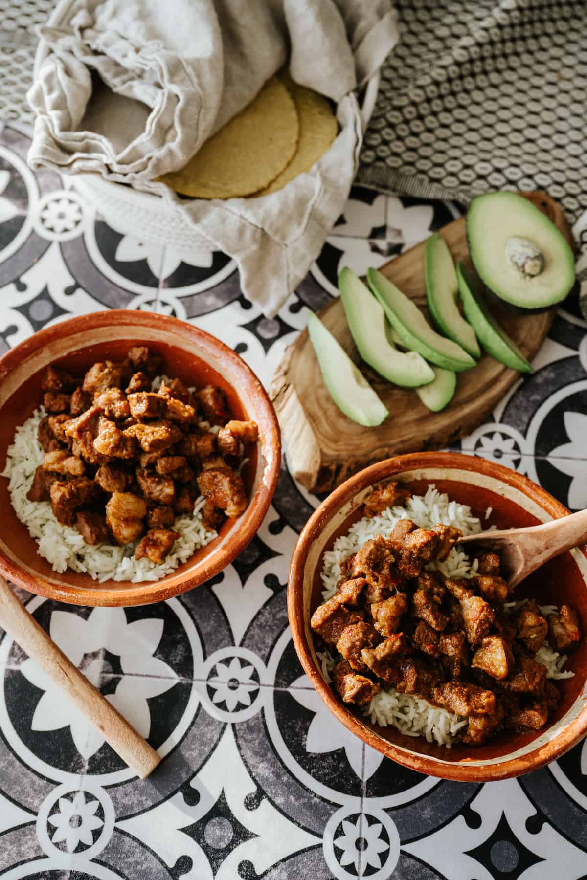 two terracotta bowls filled with steamed rice and carne adovada New Mexico-style pork stew with red chiles on a black and white patterned tile tabletop.