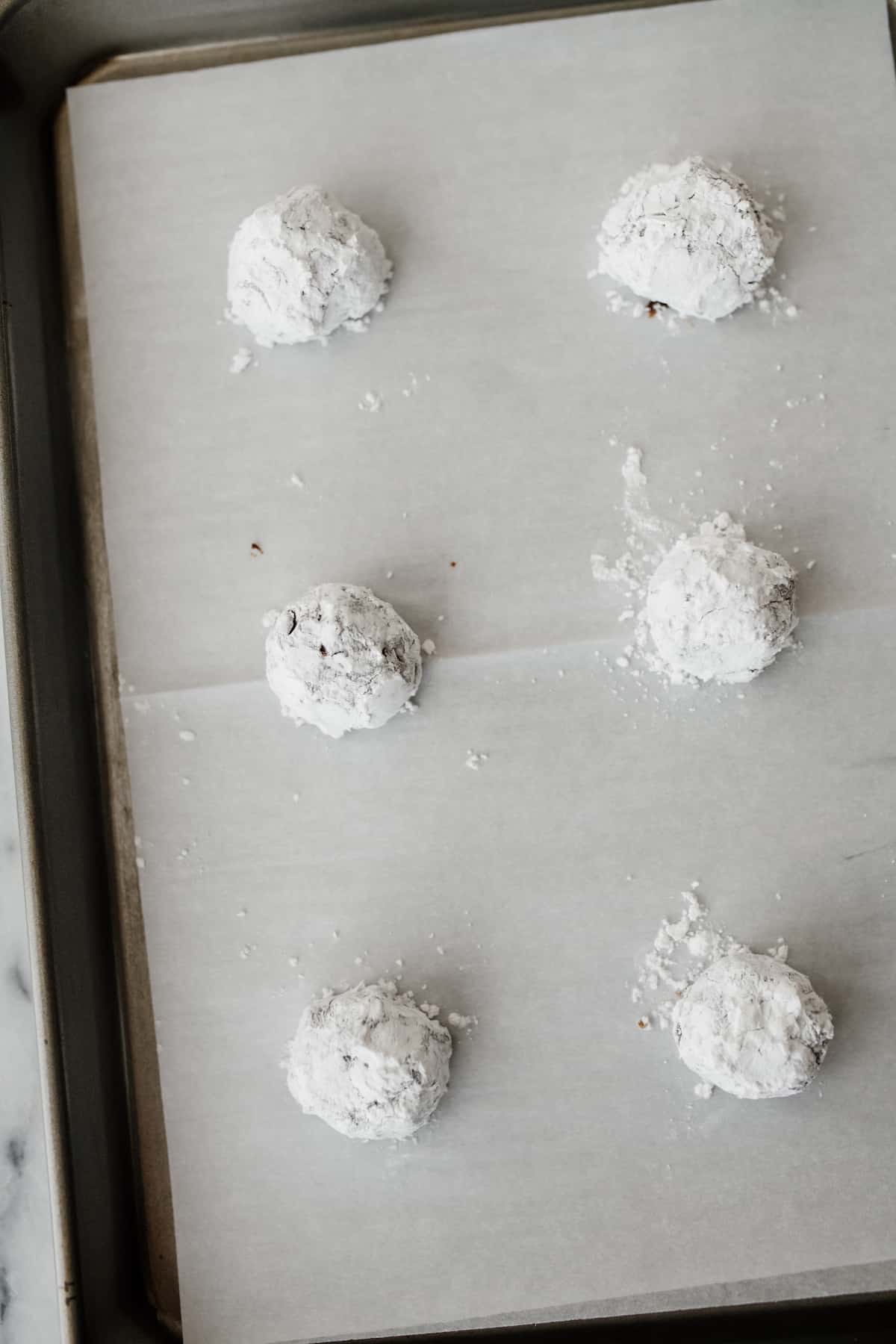 mexican chocolate crinkle cookie dough balls on a parchment-lined cookie sheet.