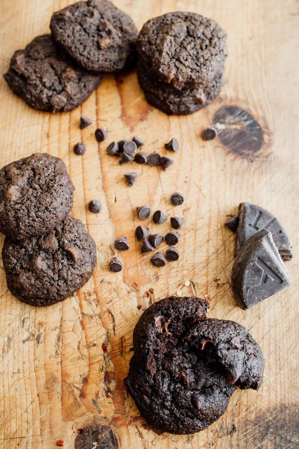 wooden cutting board topped with piles of Mexican hot chocolate cookies plus a scattering of chocolate chips and a broken wedge of Mexican chocolate. 