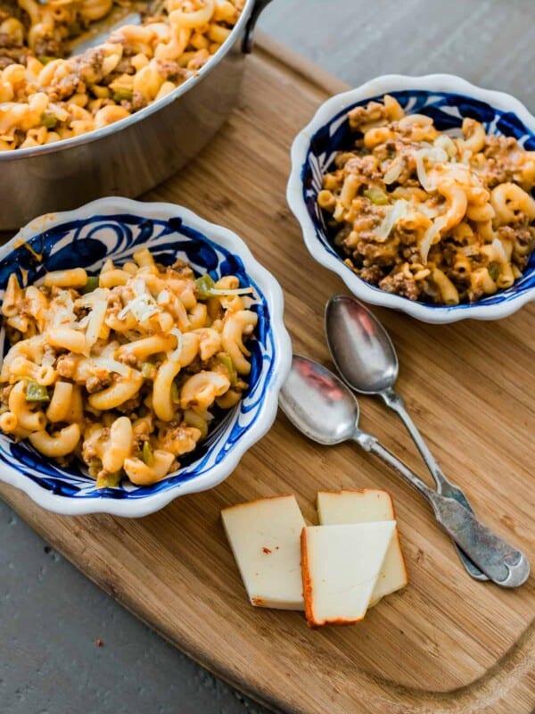 overhead shot of 2 blue and white painted bowls of meaty macaroni and cheese with ground bison on a wooden cutting board.