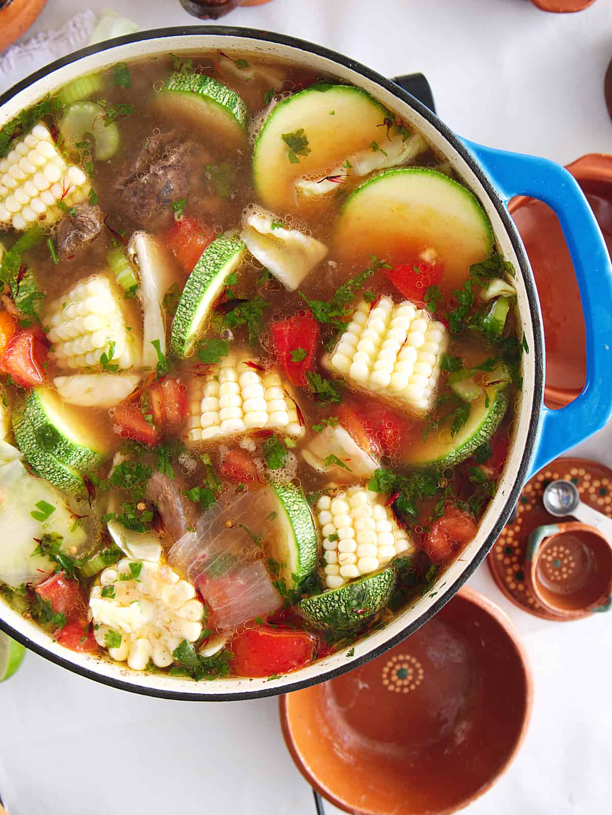 overhead shot of caldo de res beef soup in a blue enameled cast iron dutch oven.