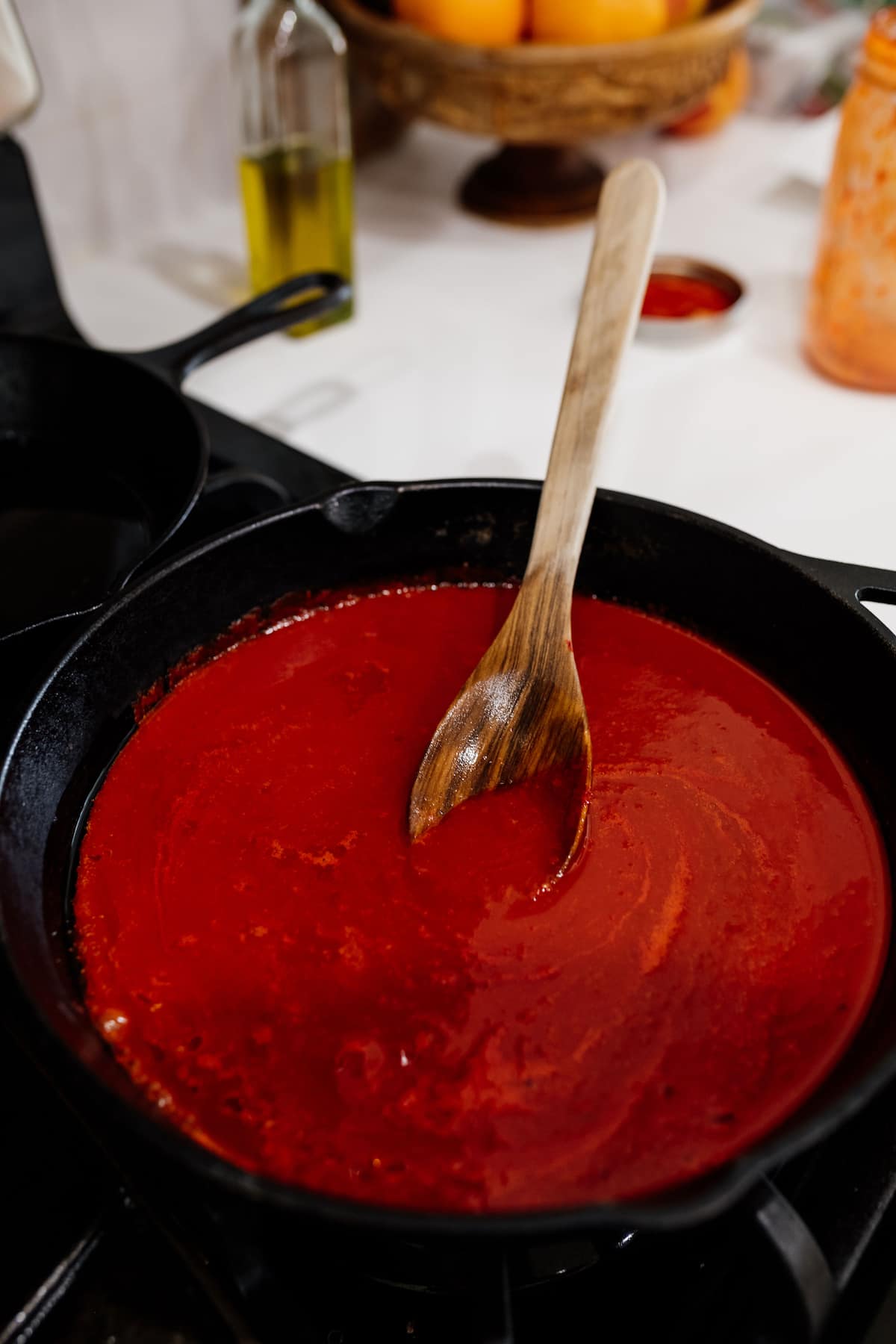 cooking red enchilada sauce in a cast iron skillet with a wooden spoon.