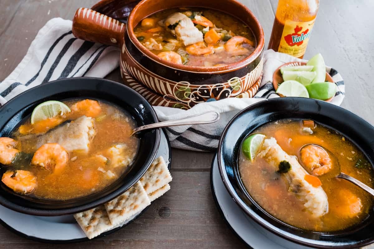 Caldo de Pescado y Camaron (Fish and Shrimp Soup) in two black bowls and crackers on the side.