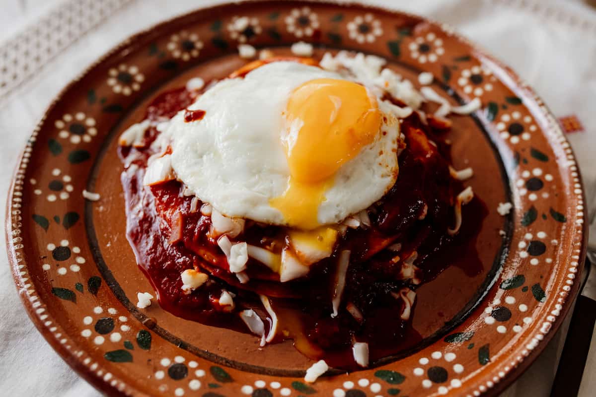 Stacked red enchiladas with a refried egg on top on a Mexican plate.