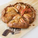 Rustic apple galette on a wooden cutting board with a silver pie server ready for slicing.