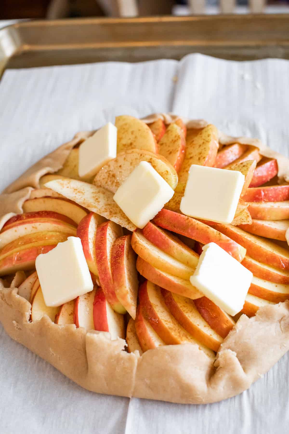 apple galette on a parchment lined sheet tray dotted with butter prior to baking.