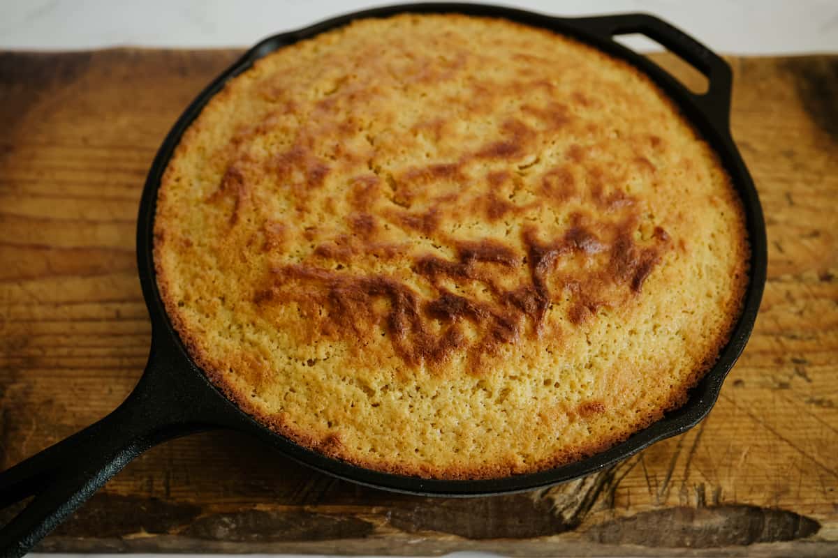 baked pastel de elote Mexican corn cake in a skillet resting on a wooden cutting board.
