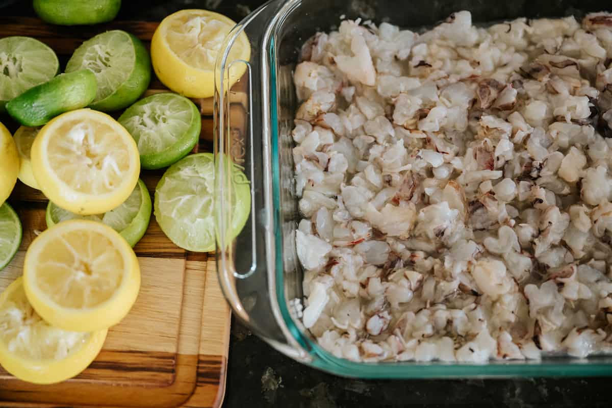 shrimp is beginning to turn opaque in the baking dish as the citrus juice works its magic. spent lemon and lime halves are to the side.