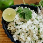 Cilantro lime rice recipe by Muy Bueno served in a black bowl with fresh cilantro and lime wedges.