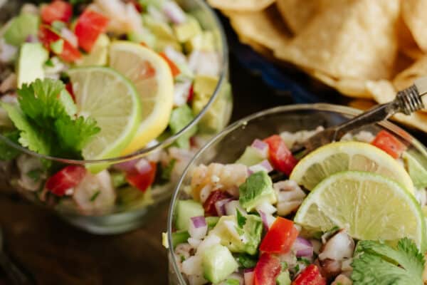 two glass goblets filled with mexican shrimp ceviche de camaron and topped with lemon and lime wedges.