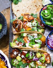 Quick & Easy Shrimp Tacos recipe served on a tray with corn tortillas, cilantro and a few bowls of garnishes on the side.