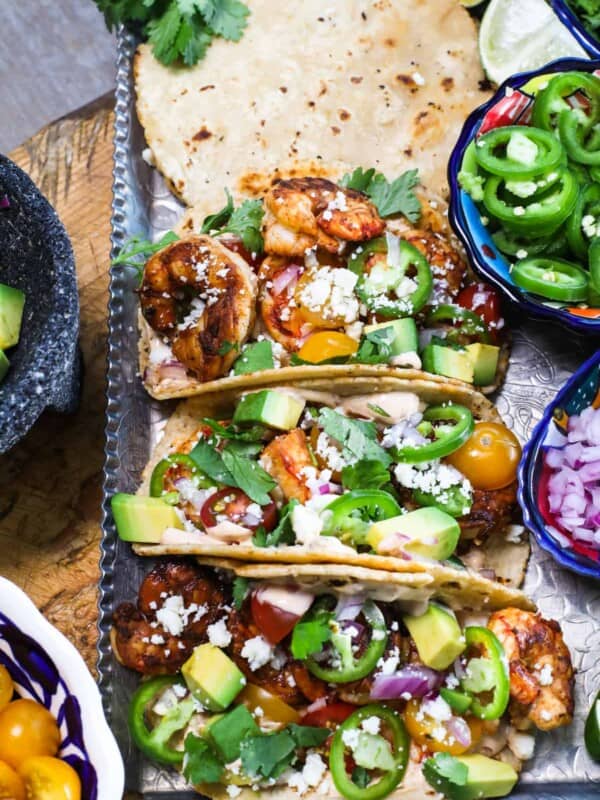 Quick & Easy Shrimp Tacos recipe served on a tray with corn tortillas, cilantro and a few bowls of garnishes on the side.