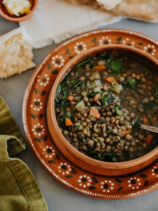 Bowl of Mexican Lentil Soup (Sopa de Lentejas) served on a terracotta plate with bread, from the Muy Bueno recipe by Yvette Marquez-Sharpnack.