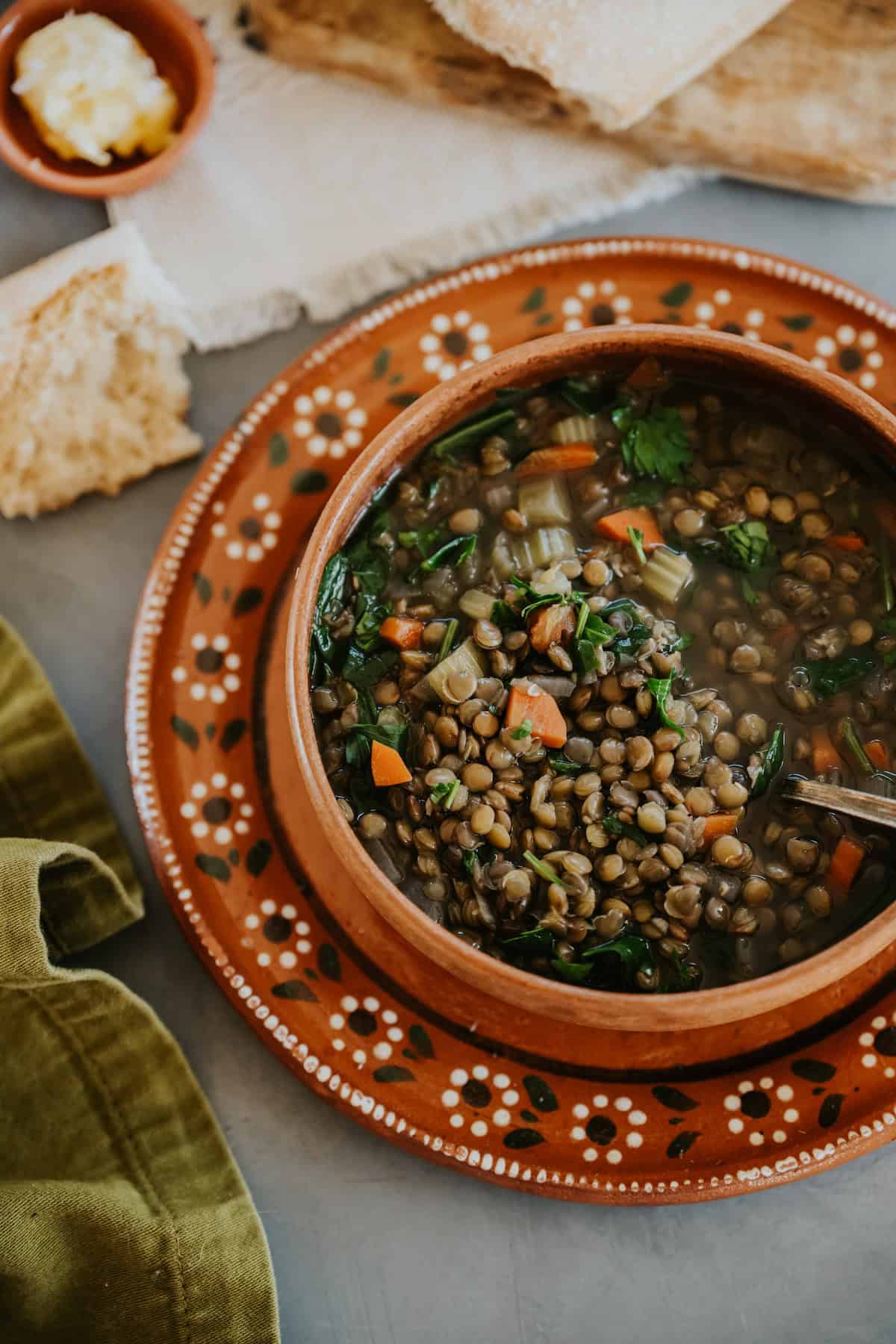 Bowl of Mexican Lentil Soup (Sopa de Lentejas) served on a terracotta plate with bread, from the Muy Bueno recipe by Yvette Marquez-Sharpnack.
