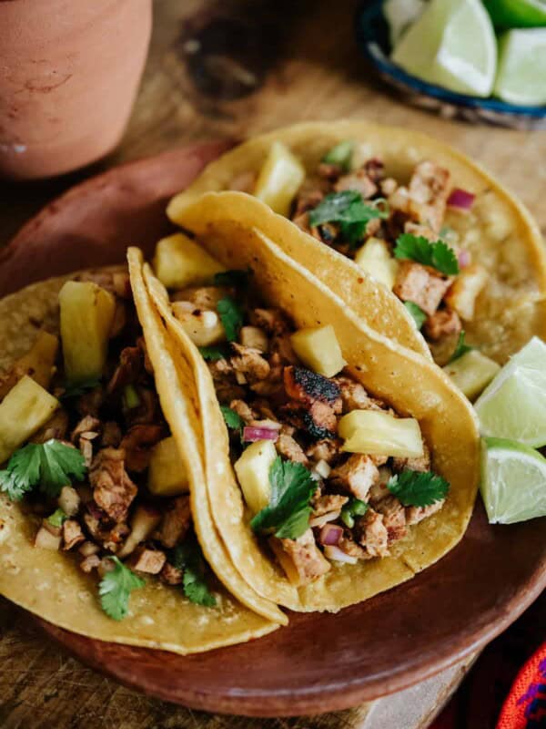 closeup shot of 3 pineapple pork tacos al pastor on an earthenware plate.