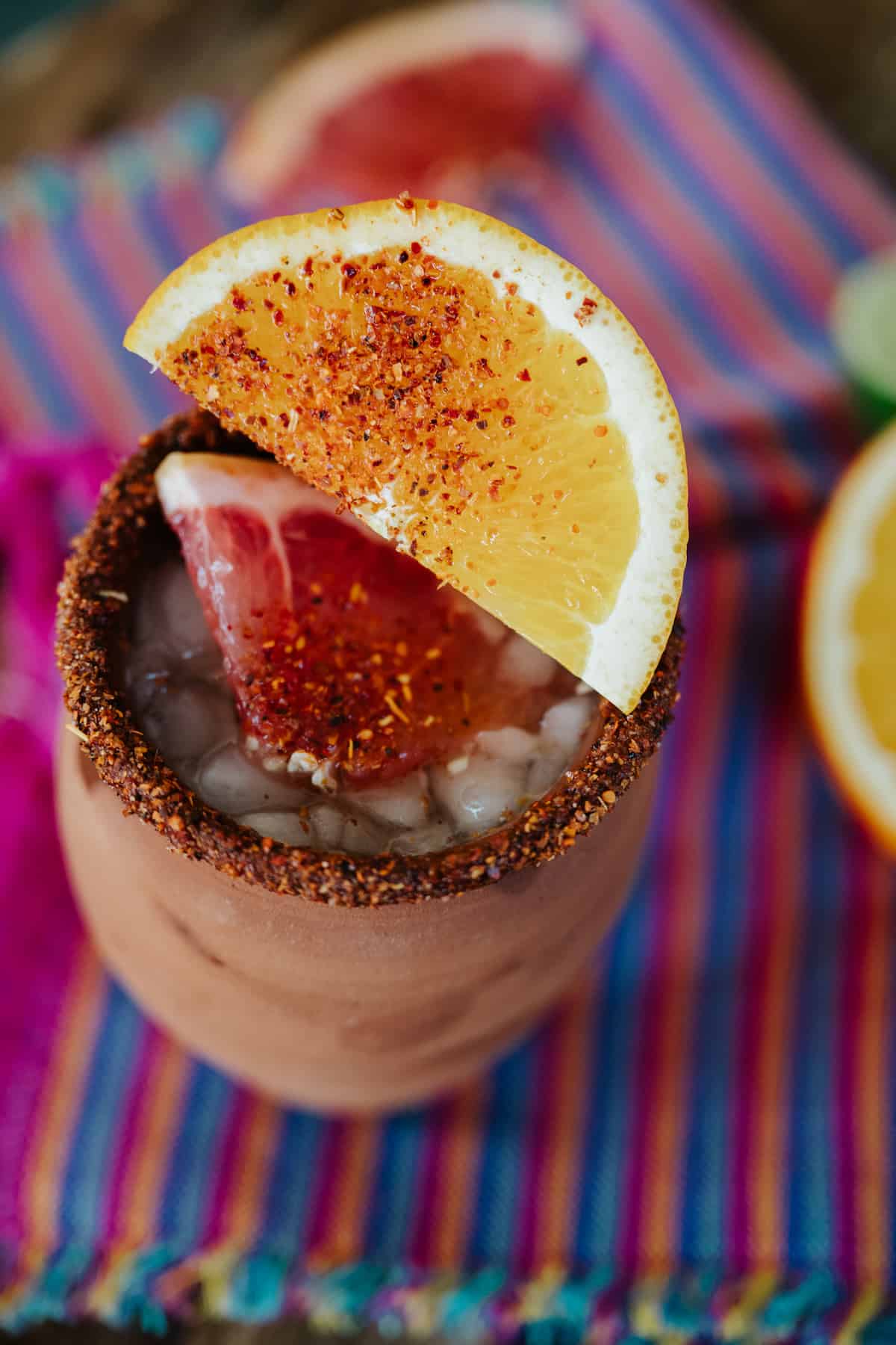 overhead shot of a skinny cantarito cocktail garnished with tajin and fresh citrus slices.