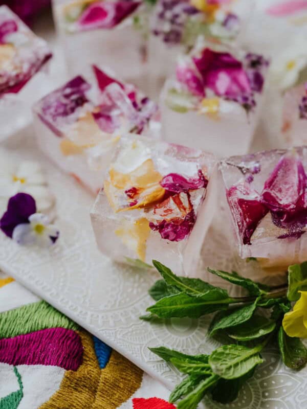 45 degree angle shot of edible flower ice cubes on a white tray next to a sprig of mint.