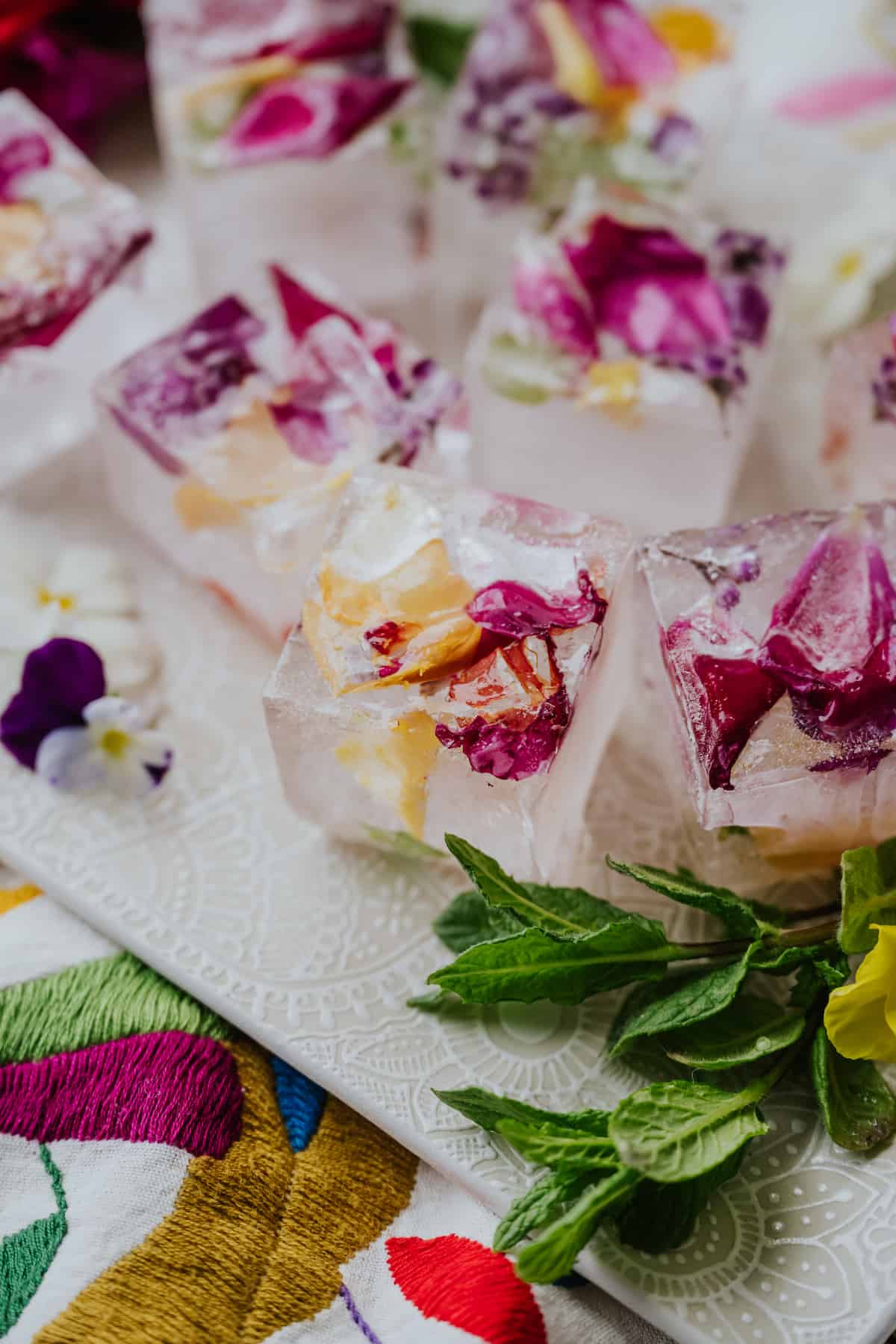 45 degree angle shot of edible flower ice cubes on a white tray next to a sprig of mint.