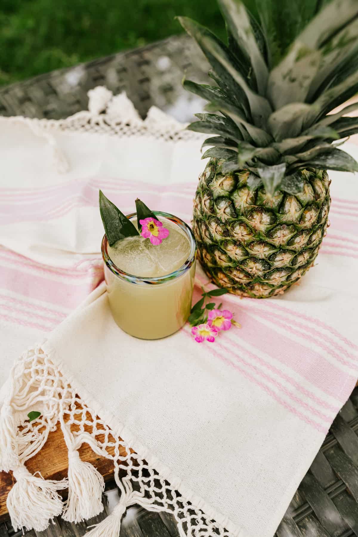 45 degree angle shot of pineapple tequila spritzer in a short rocks glass on a picnic blanket next to a whole pineapple. 