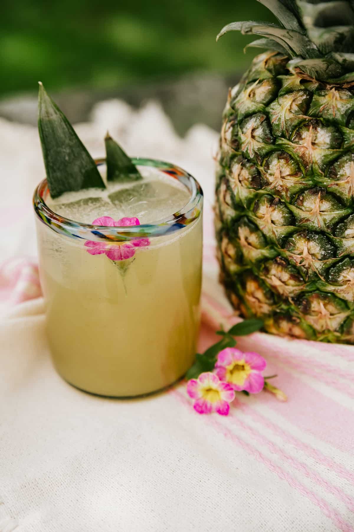 short rocks glass filled with pineapple tequila spritzer garnished with an edible flower and two fronds from a pineapple.