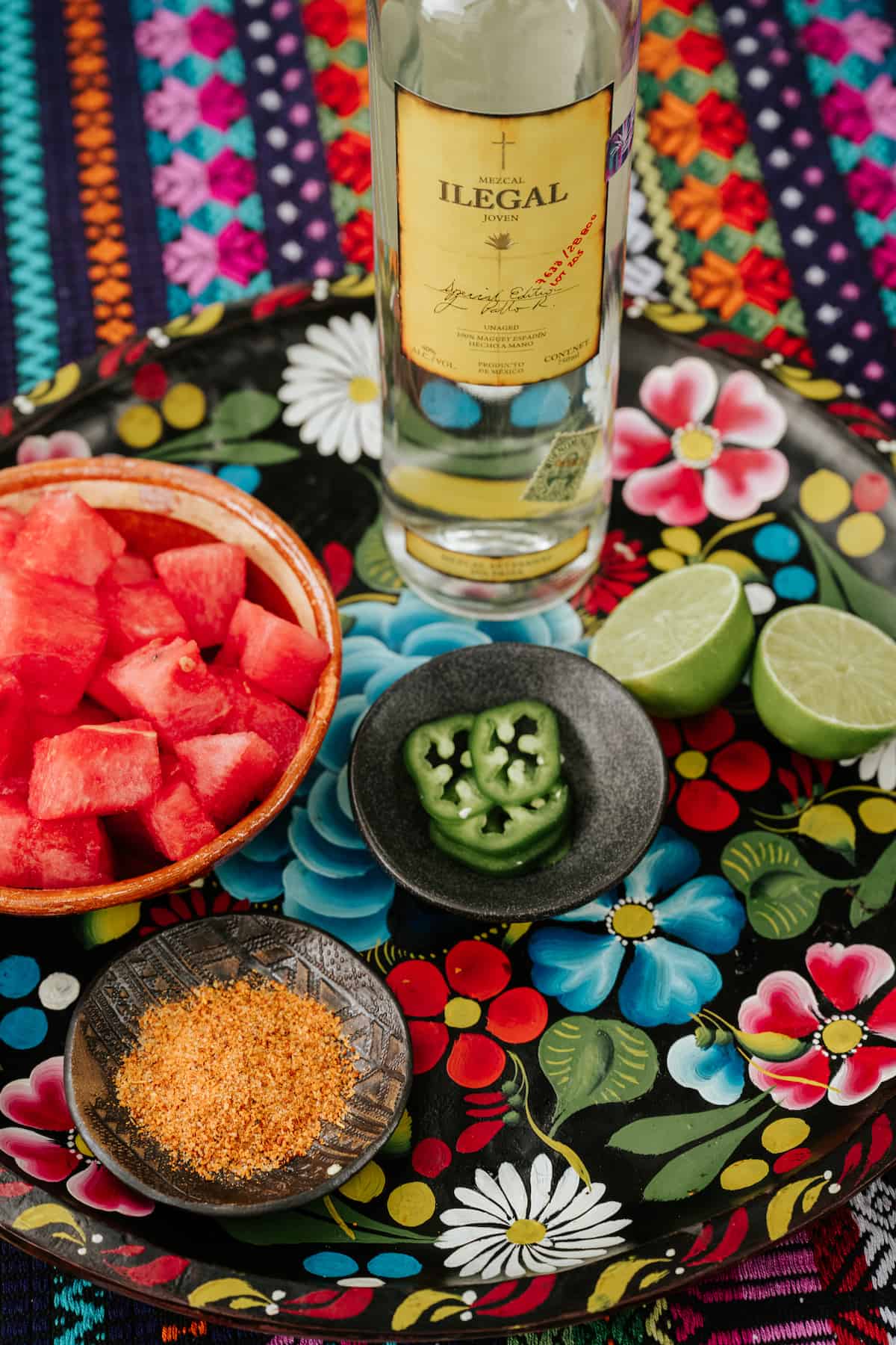 ingredients needed to make a spicy mezcal margarita with jalapeno and watermelon measured out on a hand-painted floral tray.
