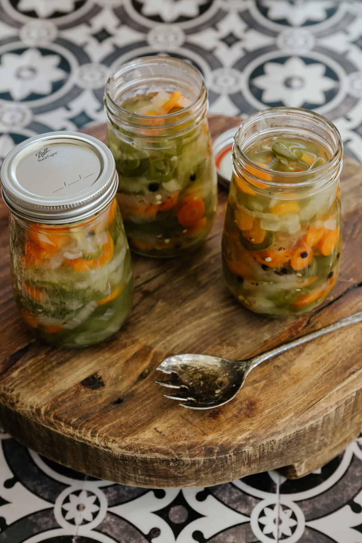 45 degree angle of jars of Mexican escabeche lined up on a wooden surface.