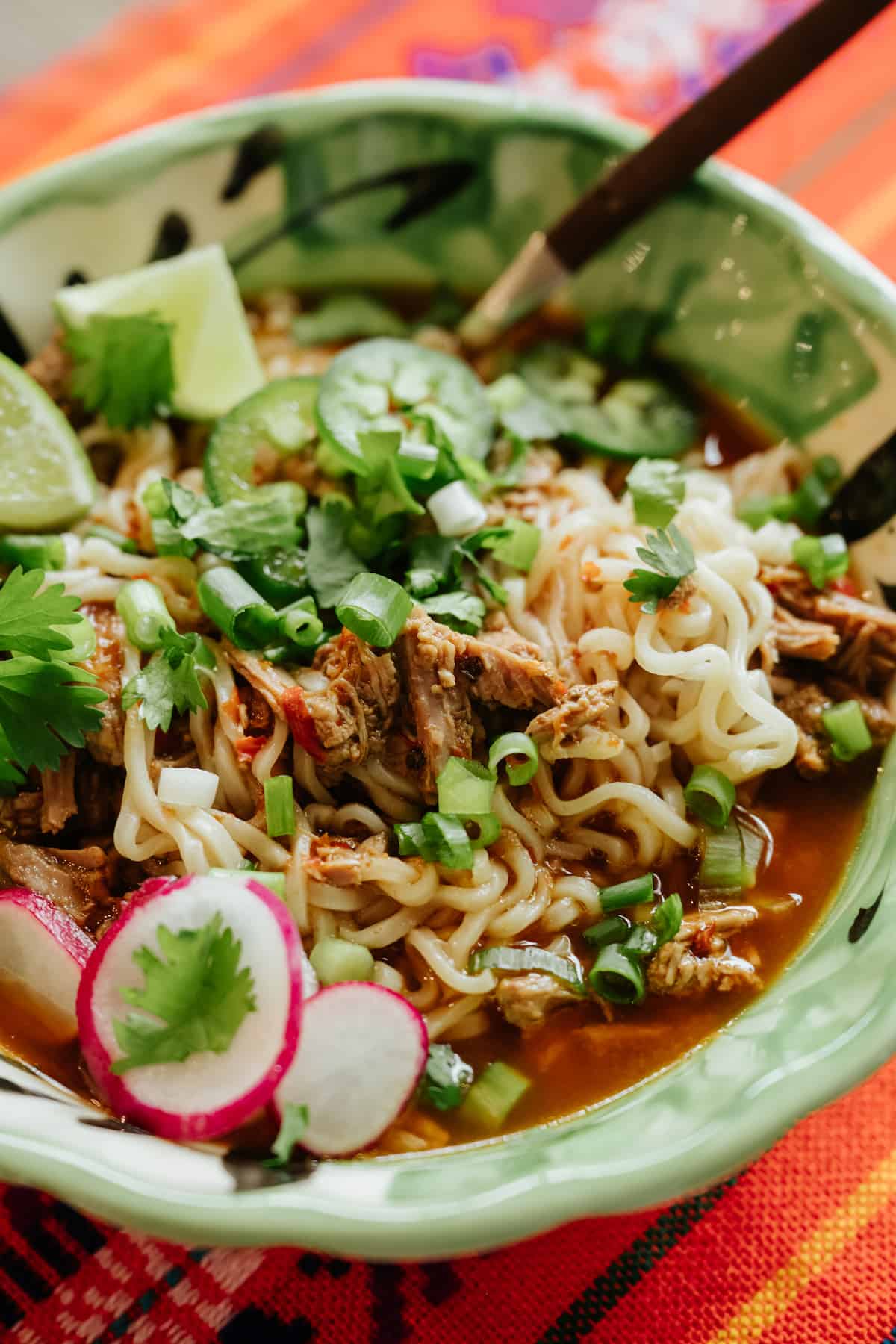green and white bowl filled with mexican ramen with birria, cilantro, scallions, and radishes.