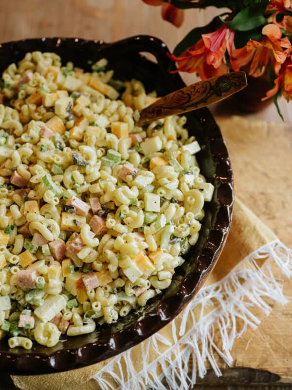 overhead shot of a hand thrown brown serving bowl filled with dill pickle macaroni salad with cheese and spam.