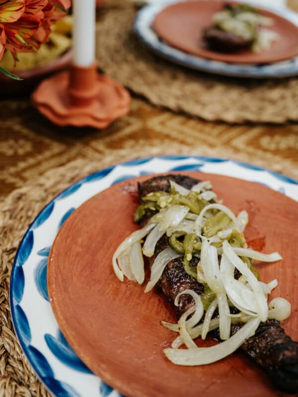 terracotta plate with a serving of tampiqueña steak topped with caramalized onions and roasted peppers