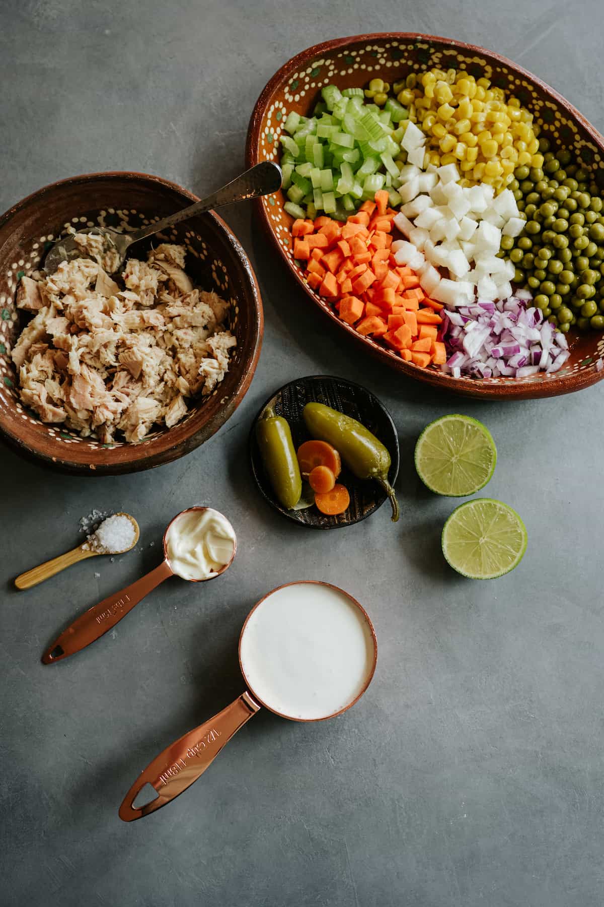 ingredients needed to make Mexican ensalada de atun (tuna saladO measured out into bowls on a grey table. 
