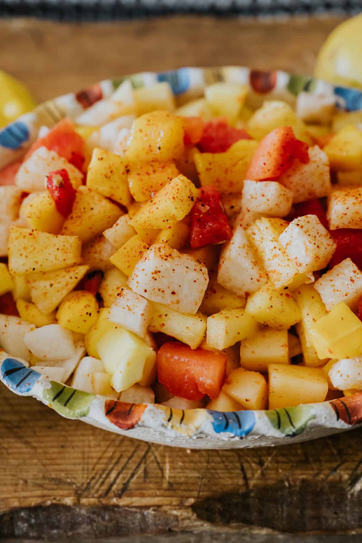 mexican fruit salad in a colorful serving bowl garnished with tajin. 