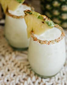 two stemless wine glasses filled with pineapple coconut margaritas and rimmed with tajin.