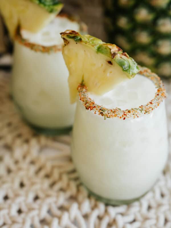 two stemless wine glasses filled with pineapple coconut margaritas and rimmed with tajin.