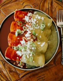 overhead shot of a dark plate with 4 enchiladas divorciadas with the left half coated in red chile sauce and the right half coated in salsa verde.