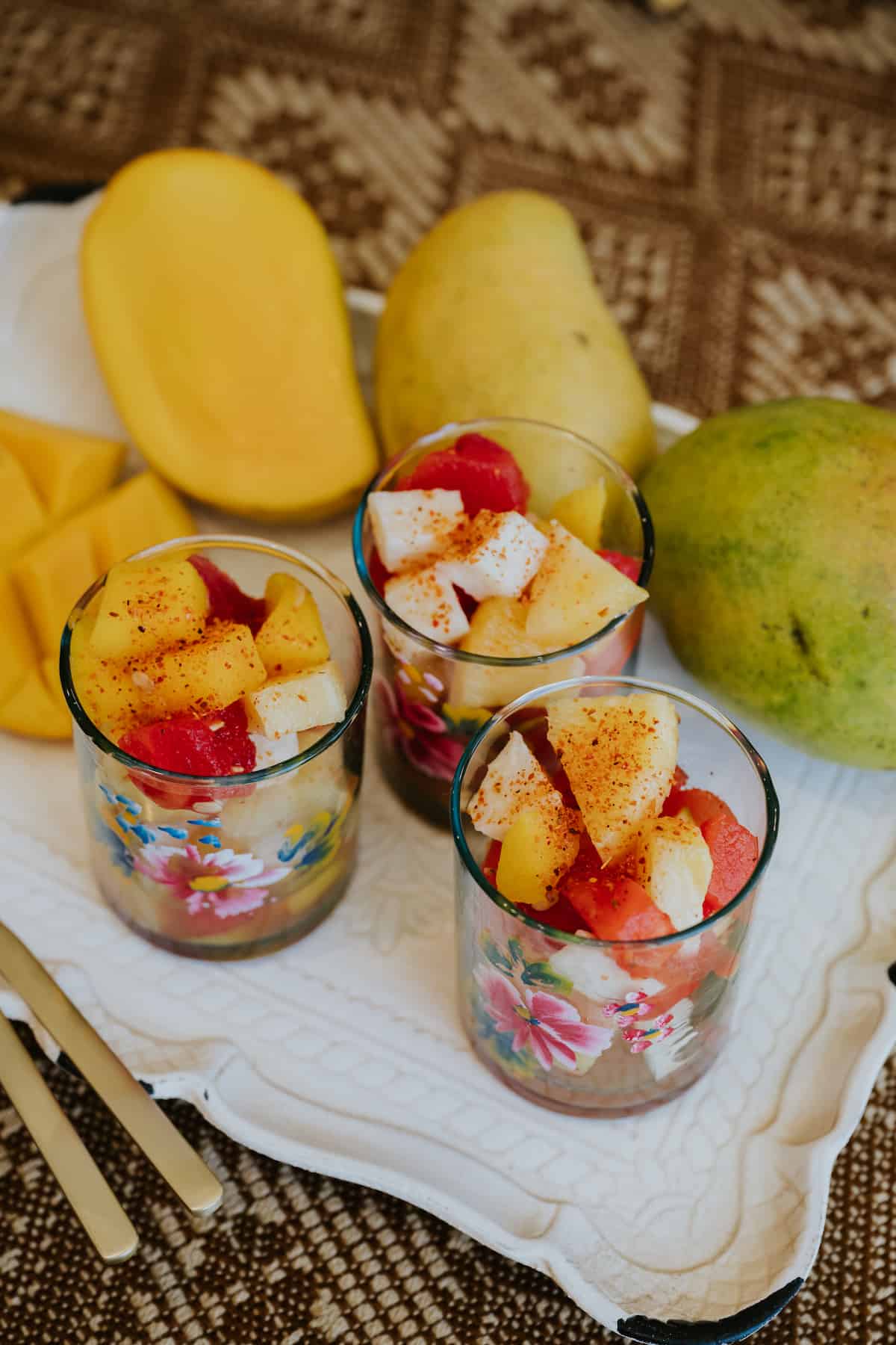 closeup shot of 3 hand-painted glasses filled with Mexican fruit salad and garnished with tajin seasoning. 
