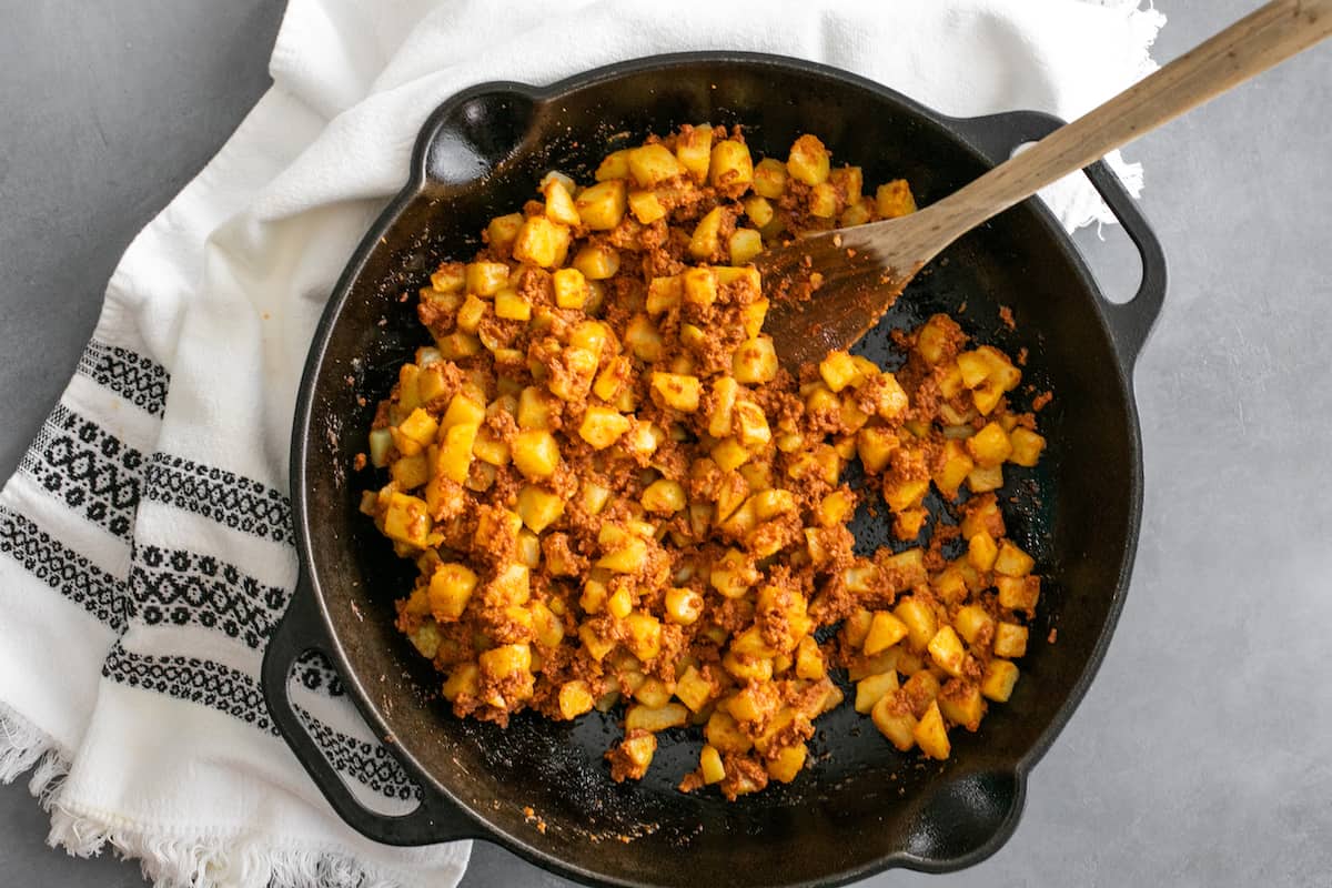 black cast iron skillet filled with a batch of papas con chorizo with a wooden spoon. 