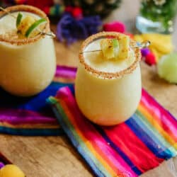 two stemless wine glasses rimmed with tajin and filled with frozen pineapple margaritas.