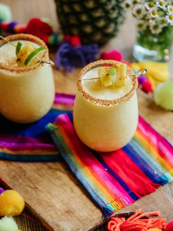 two stemless wine glasses rimmed with tajin and filled with frozen pineapple margaritas.